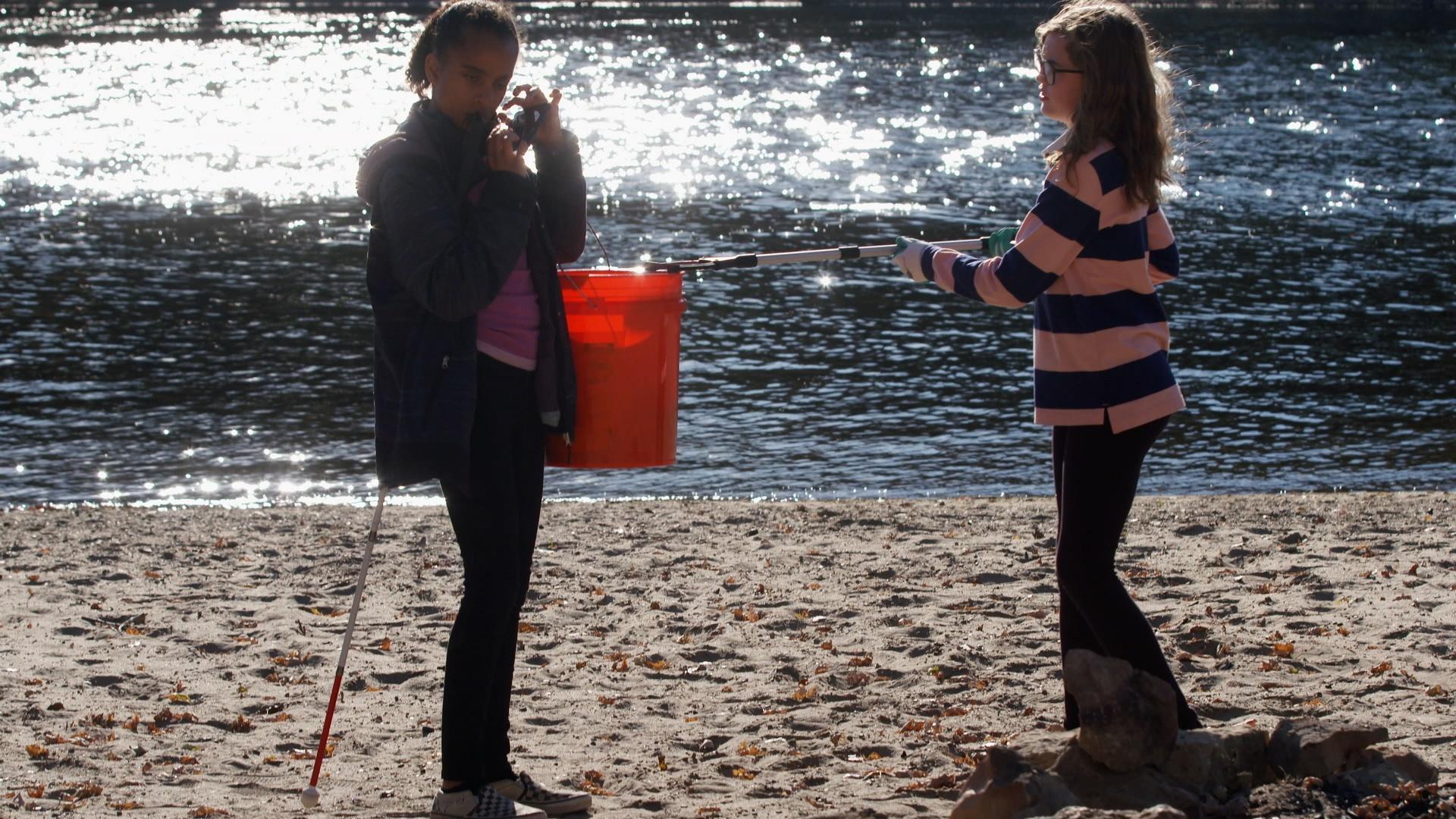The SciGirls pick up trash and gather data at a riverside park.