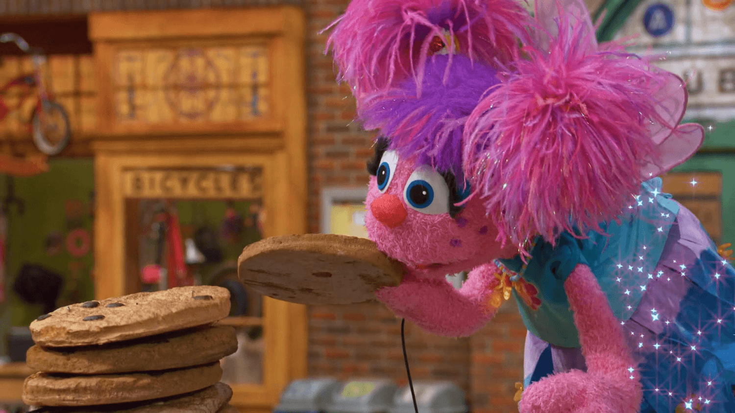 Elmo tries setting a cookie tower record while Grover takes a photo of Bert and Ernie.