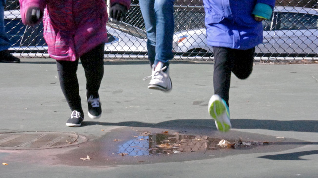 Three girls jump puddle